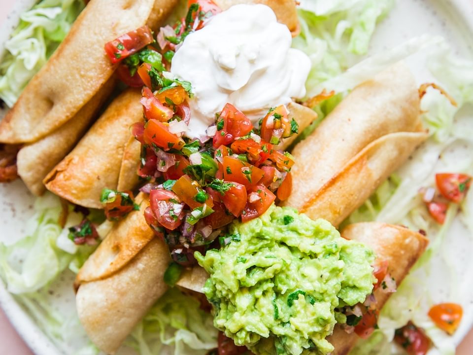 Homemade Chicken Taquitos on a plate with guacamole, sour cream and salsa