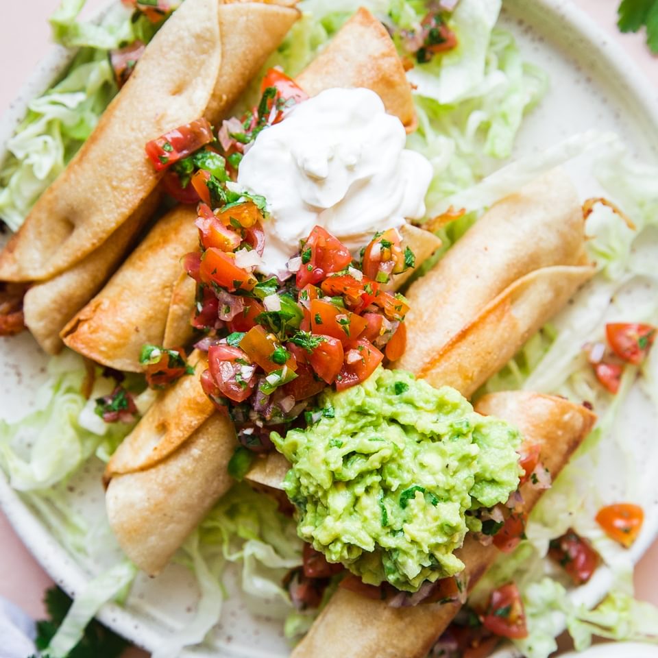 Homemade Chicken Taquitos on a plate with guacamole, sour cream and salsa