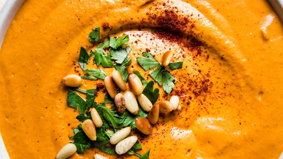 bowl of homemade romesco sauce topped with pine nuts, parsley and smoked paprika