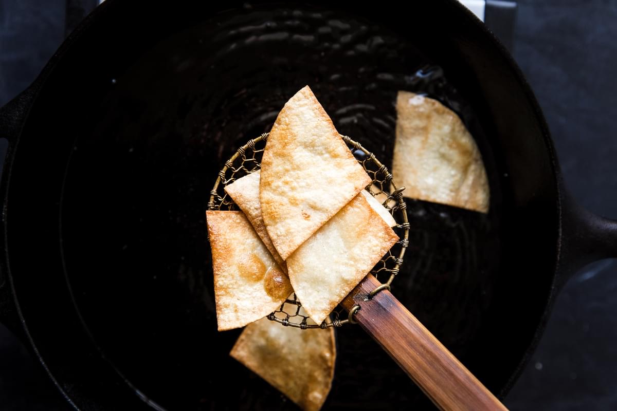 close up of freshly fried corn tortilla chips emerging from hot oil.