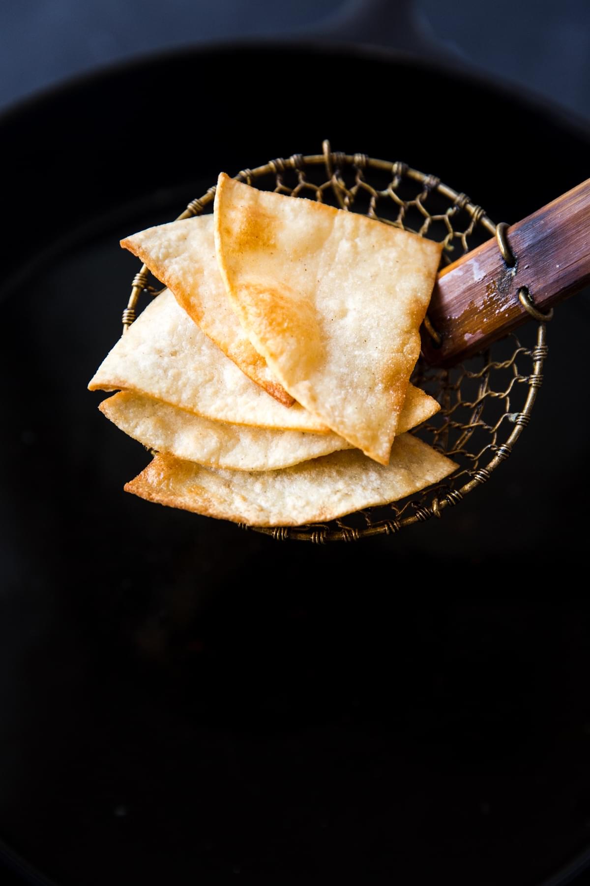 close up of freshly fried corn tortilla chips emerging from hot oil.