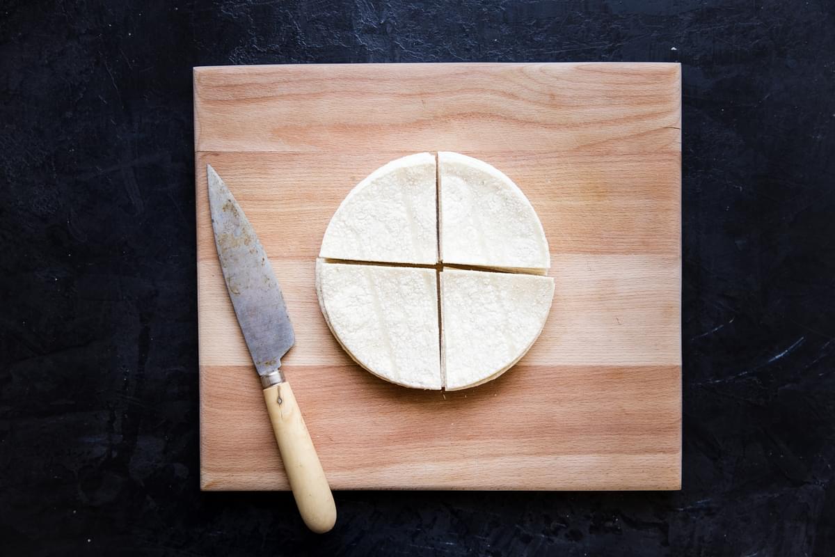 a stack of raw corn tortillas cut into quarters on a cutting board with a knife