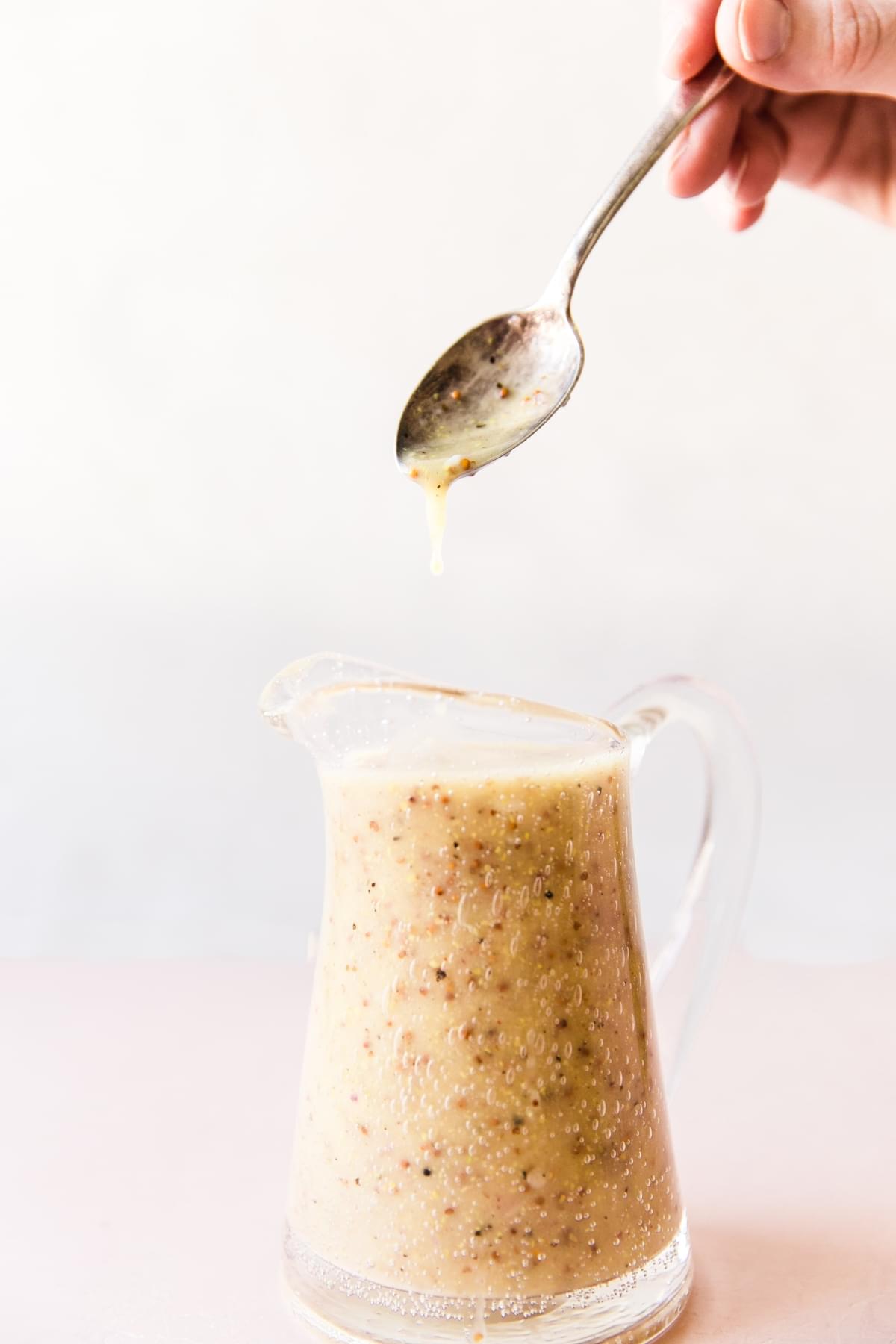 Honey Mustard Salad Dressing dripping off a spoon into a small pitcher