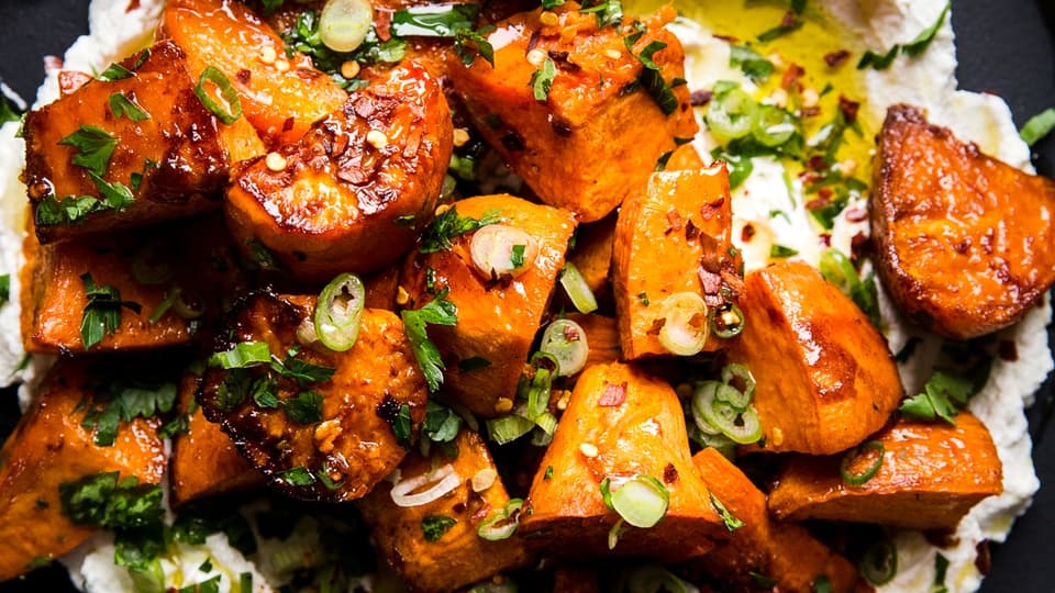 Honey Roasted Sweet Potatoes over labneh with olive oil and green onions and parsley on a plate