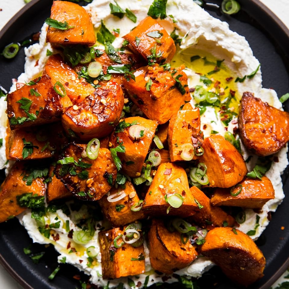 Honey Roasted Sweet Potatoes over labneh with olive oil and green onions and parsley on a plate