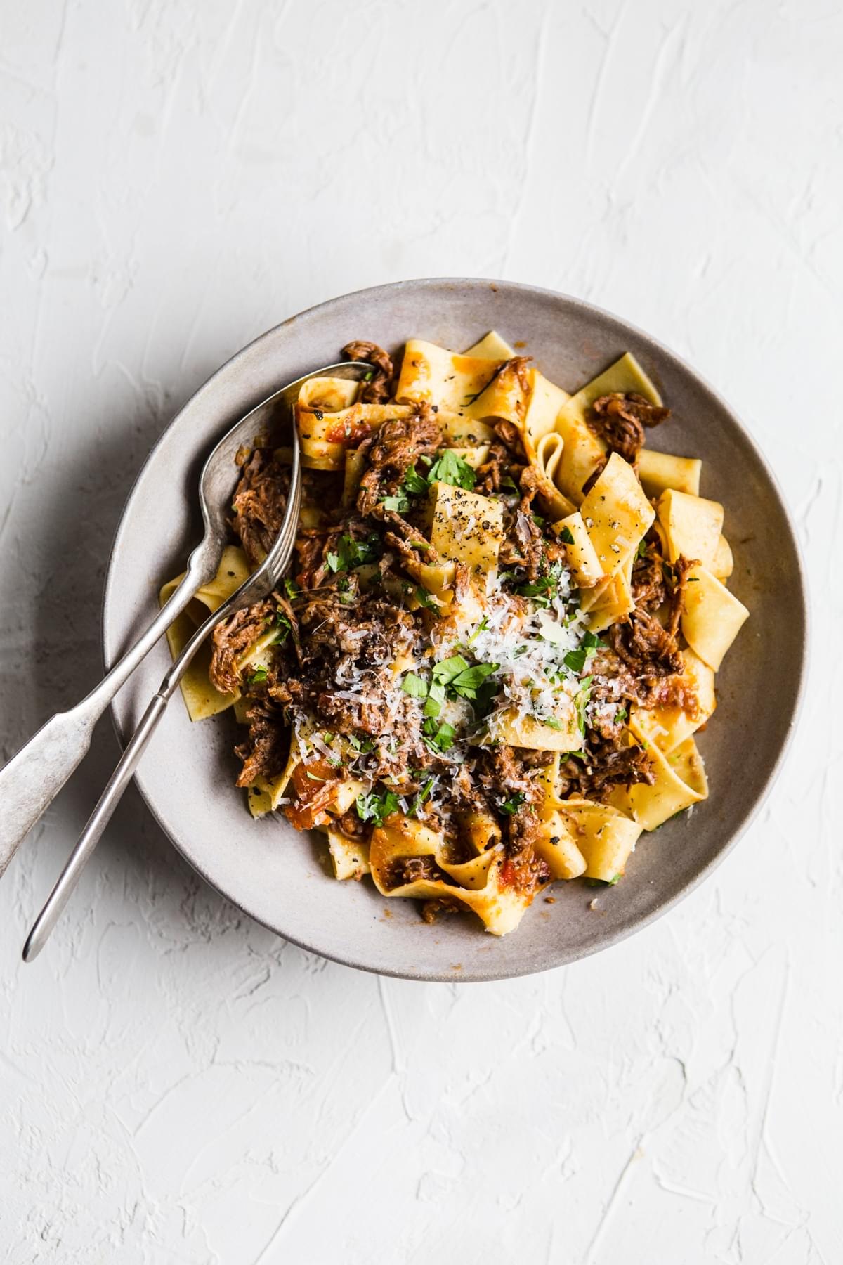 bowl of instant pot beef ragu over parrpadelle noodles with parmesan cheese and fresh parsley