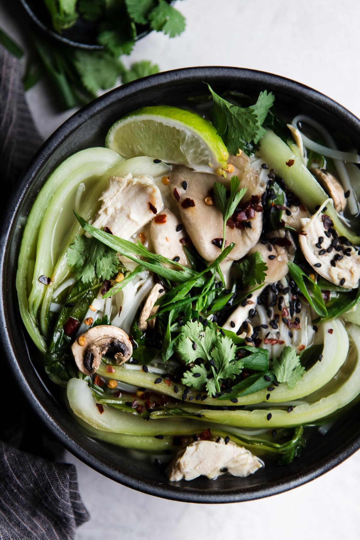 black bowl with leftover turkey soup with shallots, garlic, ginger, chicken stock, bok choy, mushrooms and rice noodles