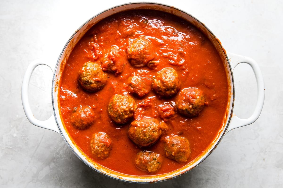 Italian meatballs simmering in a large pot filled with spaghetti sauce