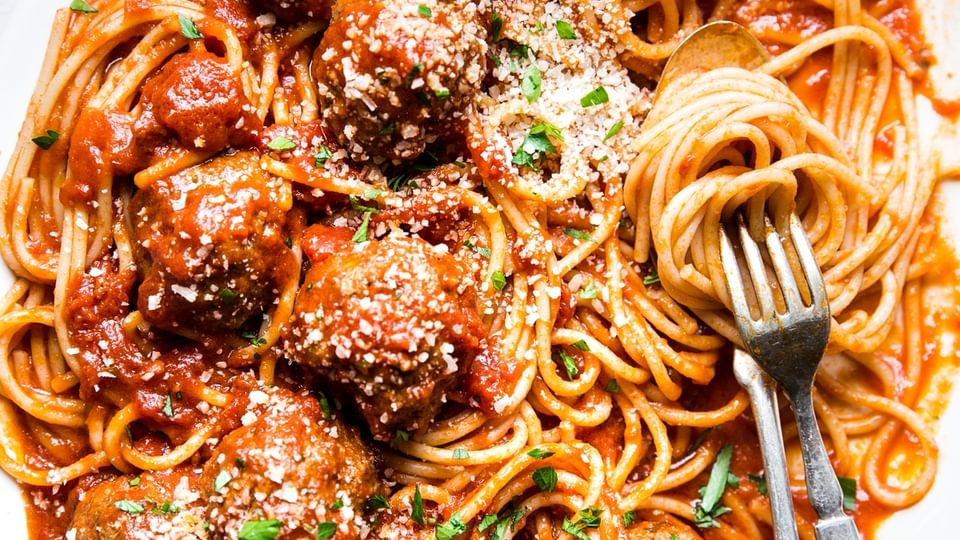 white platter of spaghetti with tomato sauce and meatballs topped with parmesan cheese and fresh parsley