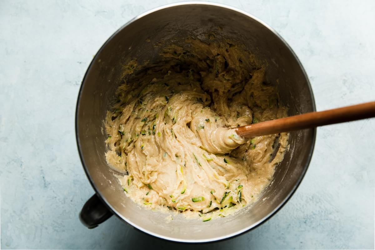 zucchini muffin batter in a mixing bowl with a wooden spoon