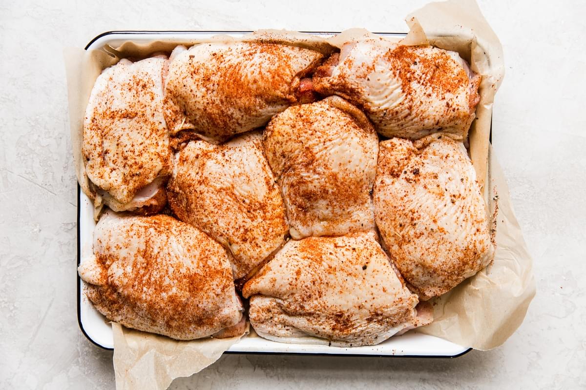 raw bone in skin on chicken thighs seasoned on metal tray lined with parchment paper