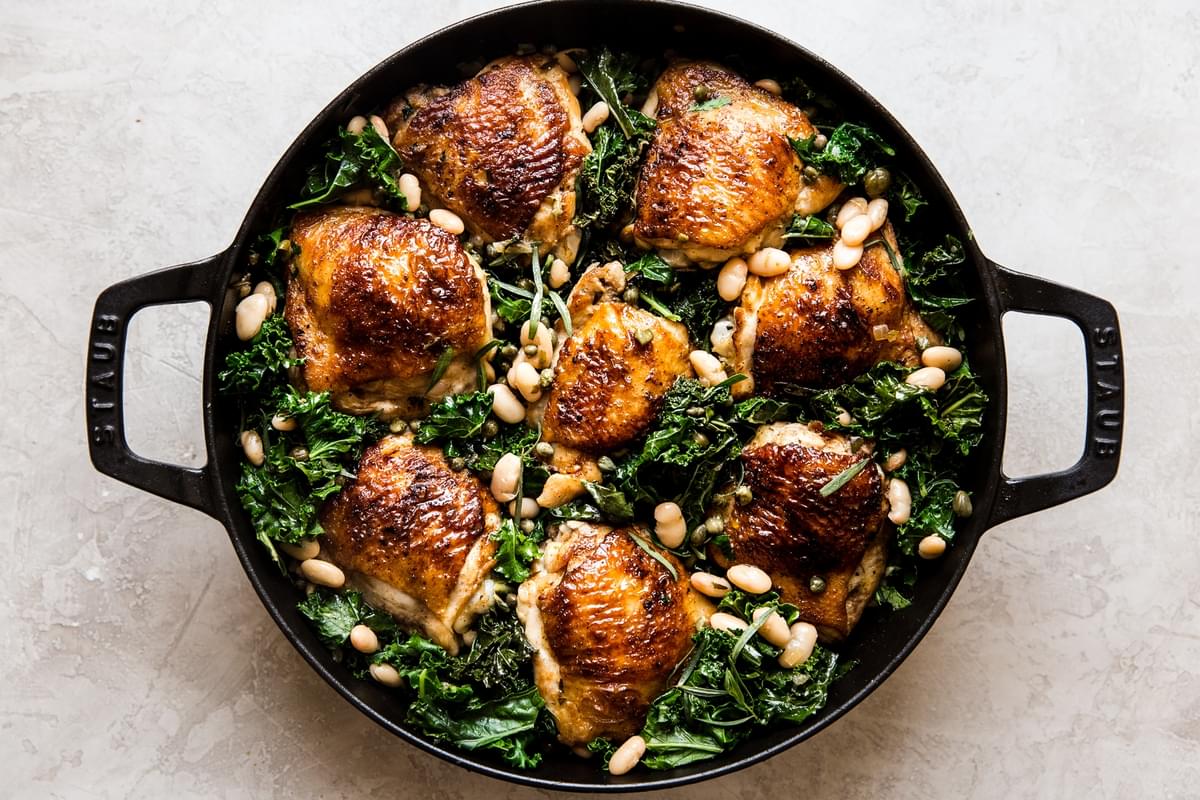cast iron braiser filled with one pot braised crispy chicken and kale with white beans