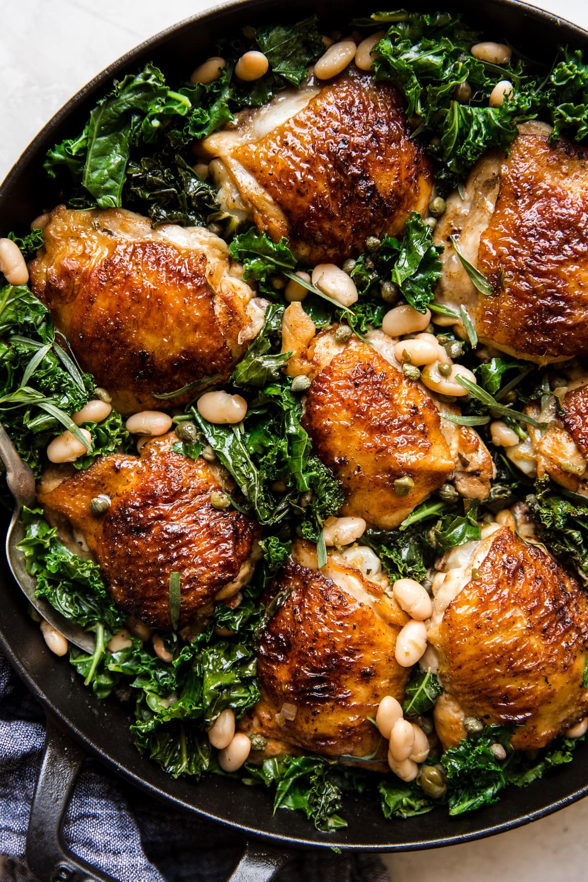 crispy chicken thighs in a cast iron skillet with kale and white beans