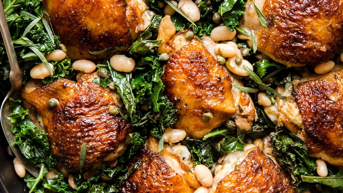 one pot braised chicken and kale with white beans in a cast iron skillet