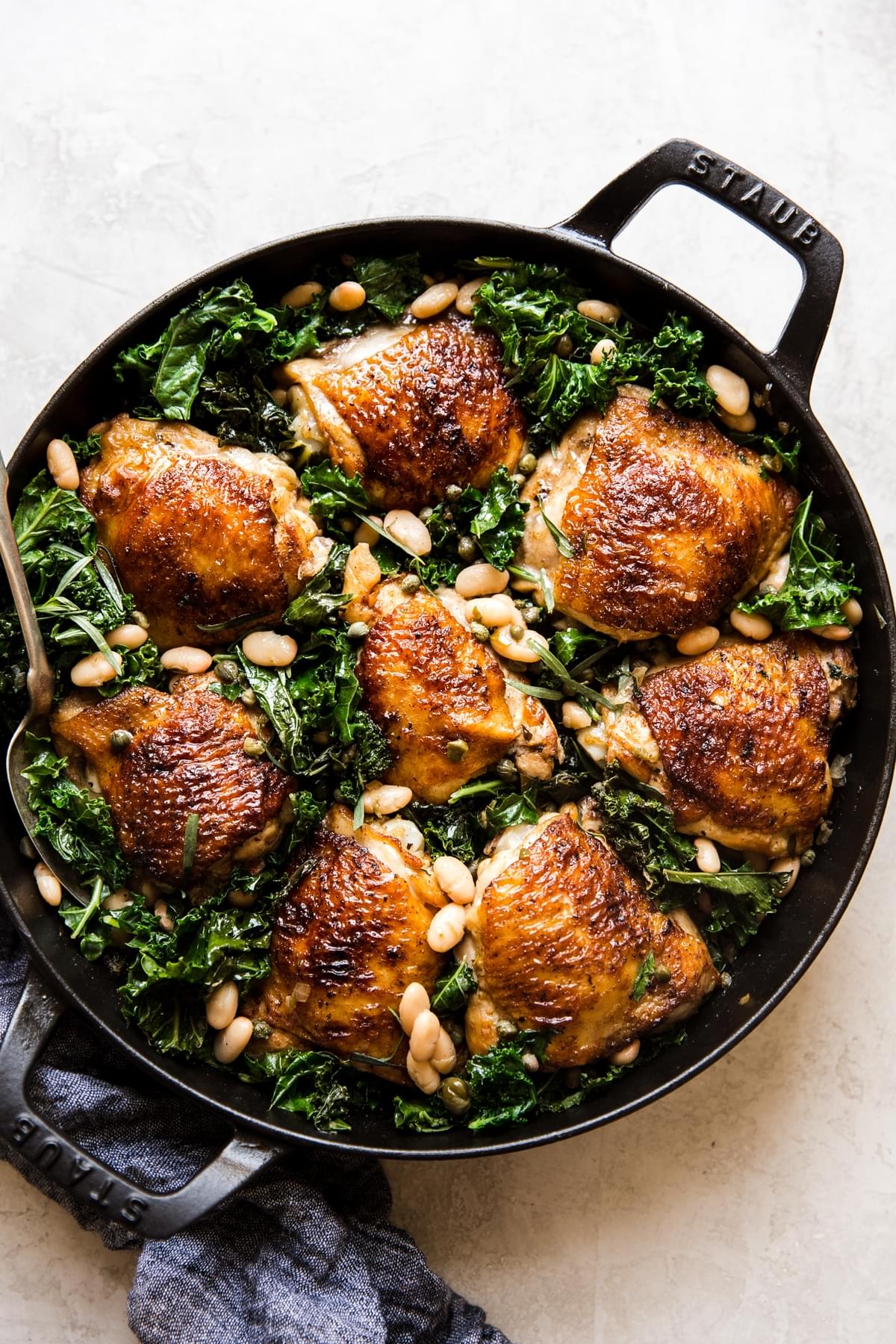 cast iron braiser with one pot braised chicken and kale with white beans
