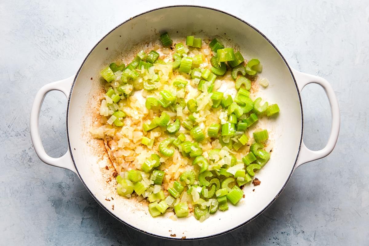 large white skillet of sautéed onions and celery for one pot chicken and stuffing casserole