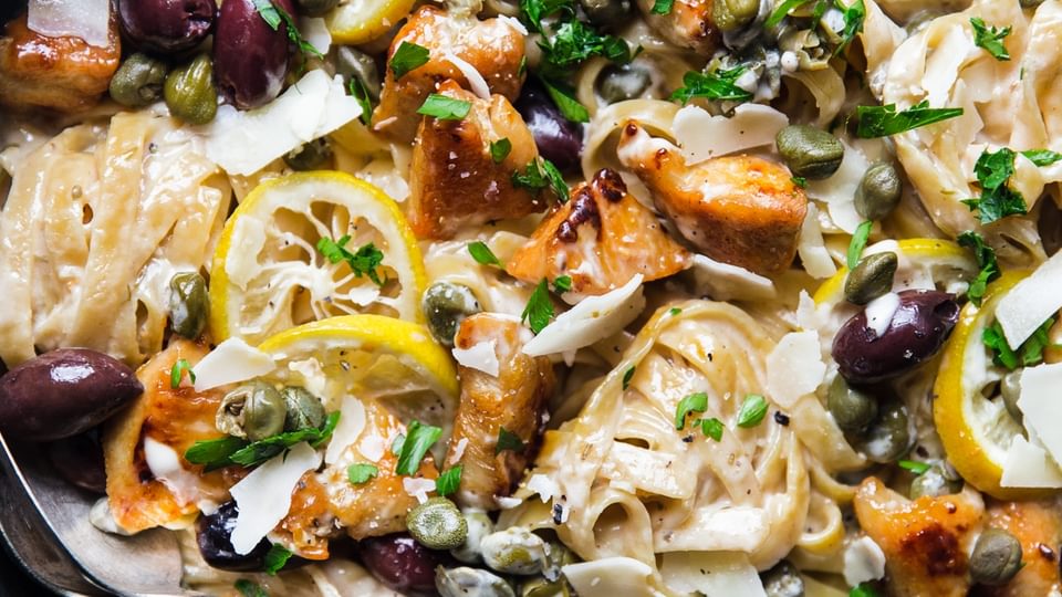 A pan filled with Mediterranean Chicken pasta, lemons and olives with a spoon
