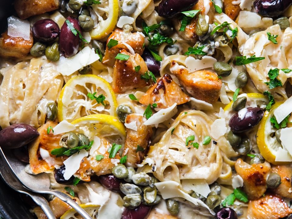 A pan filled with Mediterranean Chicken pasta, lemons and olives with a spoon