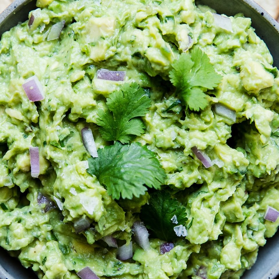 close up of guacamole in a bowl with cilantro and red onion and chips