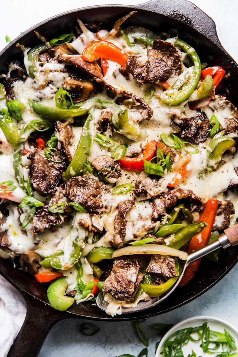 bell peppers, onions, steak and melted cheese in a cast iron skillet for a philly cheesesteak skillet