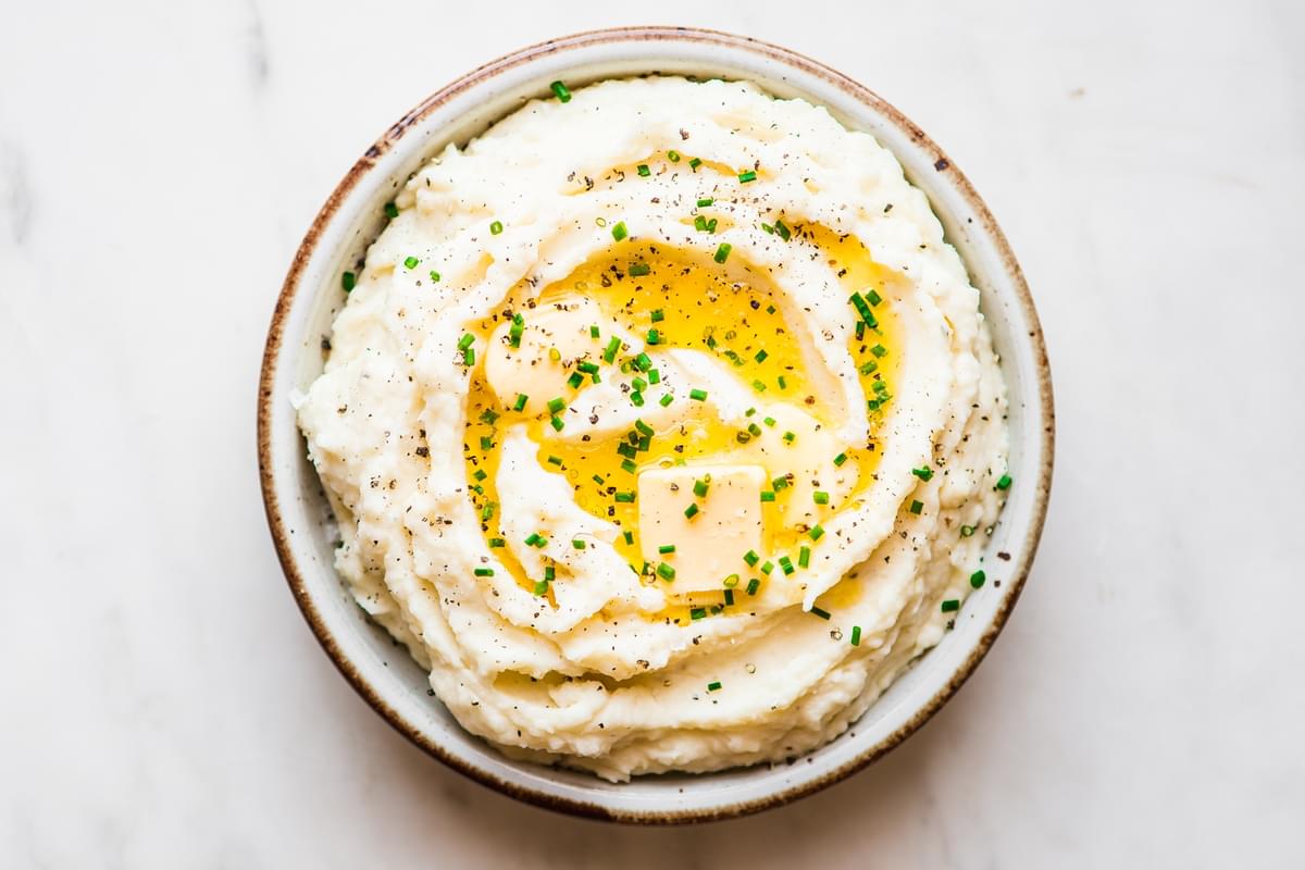 A serving bowl filled with roasted garlic mashed potatoes topped with melted butter, fresh chives and black pepper