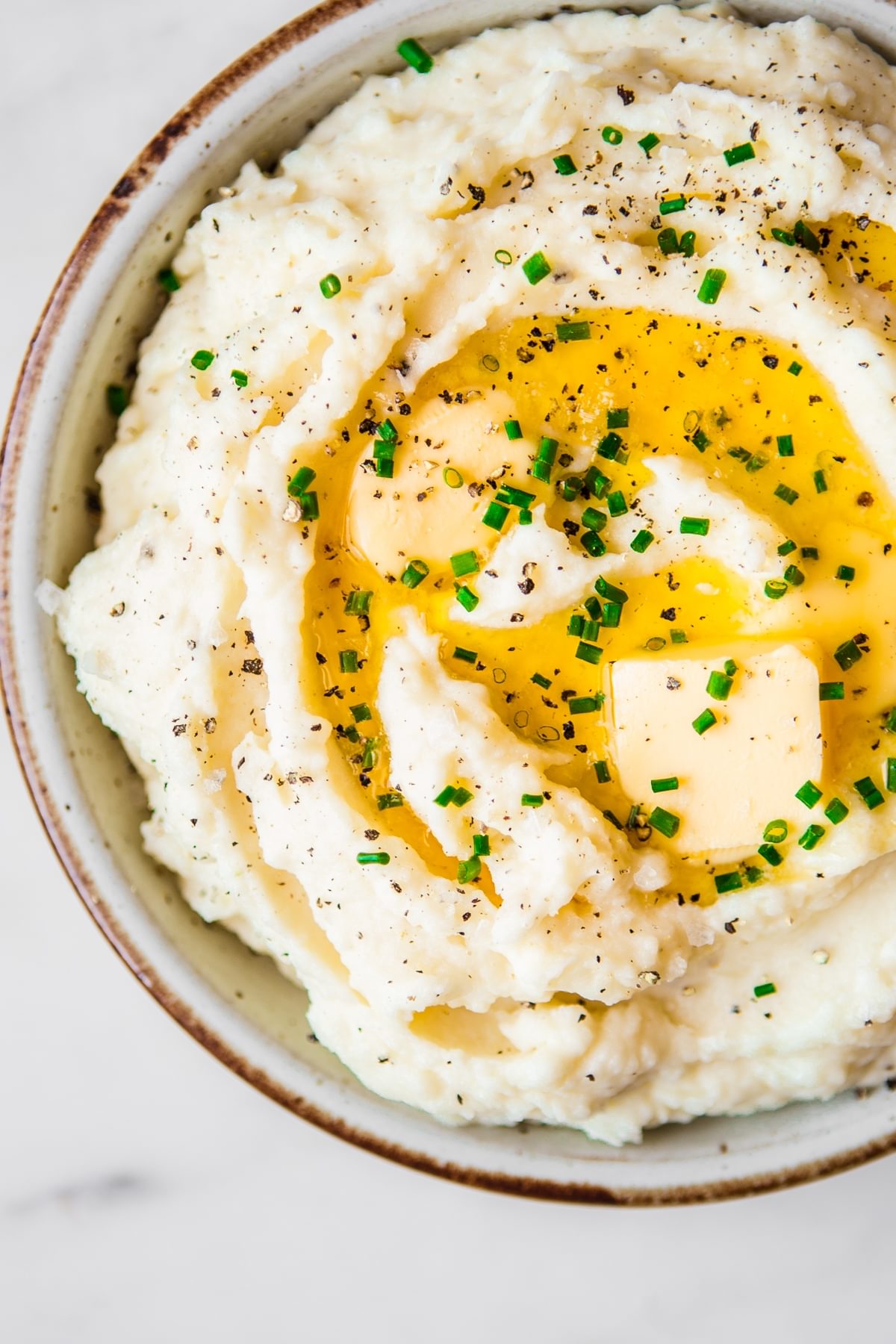 bowl of roasted garlic mashed potatoes topped with melted butter, fresh chives and black pepper