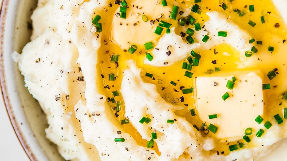 bowl of roasted garlic mashed potatoes topped with melted butter, fresh chives and black pepper