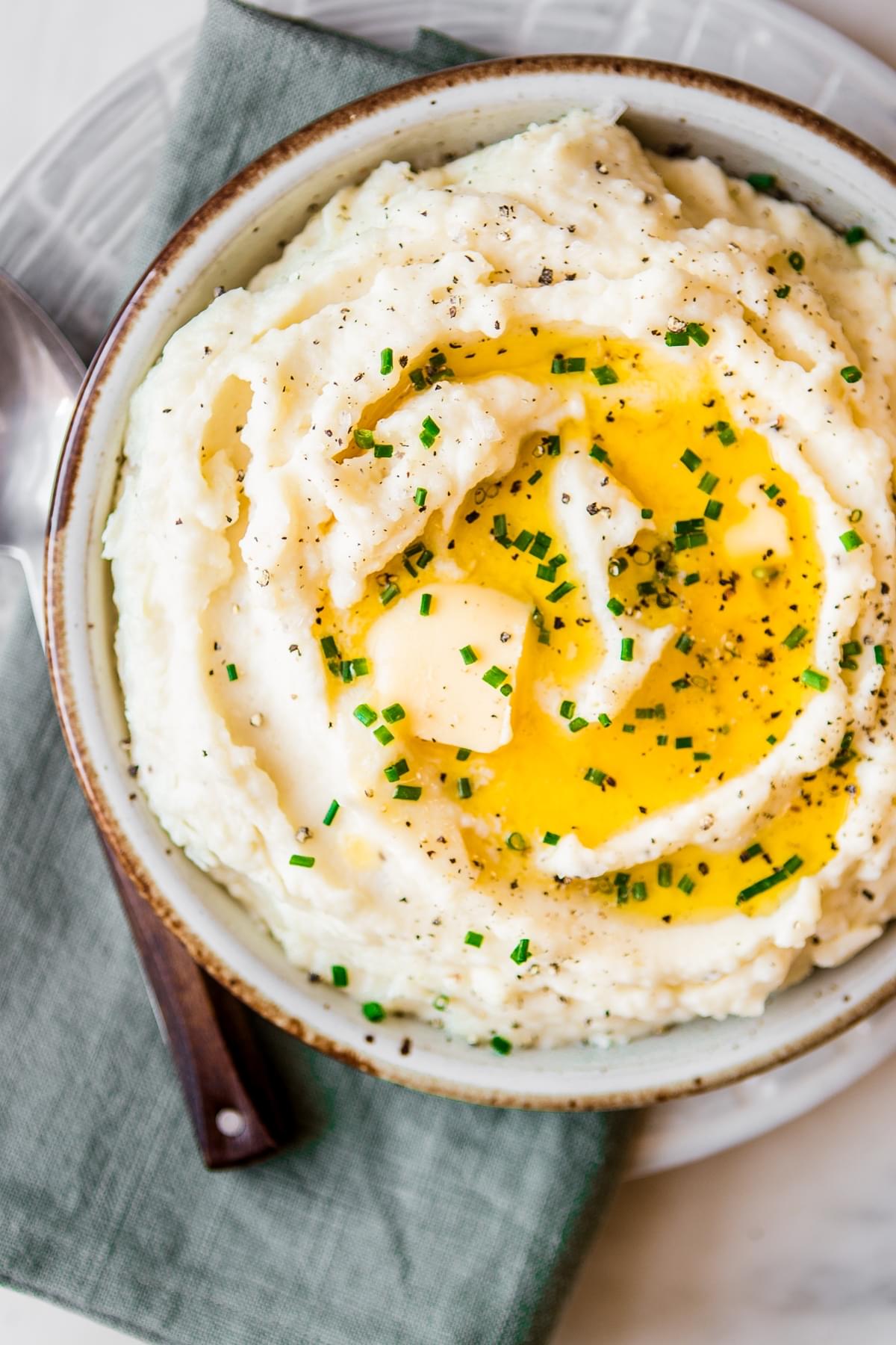 A bowl of roasted garlic mashed potatoes topped with melted butter, fresh chives and black pepper on a plate