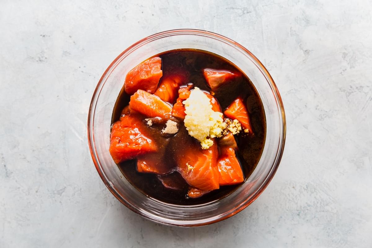 large cubes of salmon in a glass bowl with brown sugar, soy sauce, garlic and fresh ginger