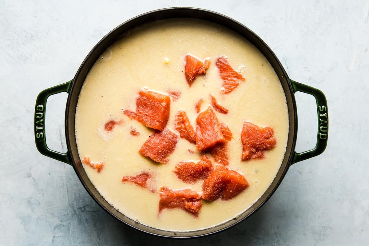 raw salmon added to a creamy base in a large pot for salmon chowder