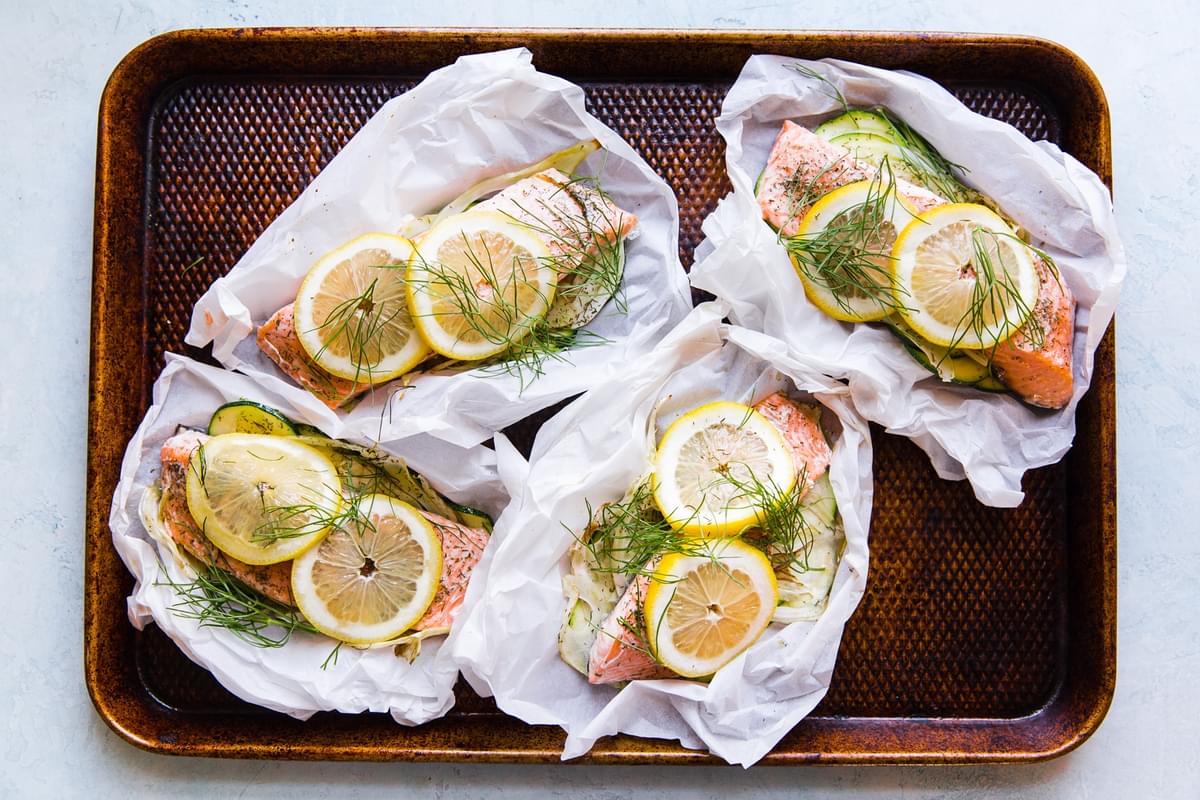 salmon in parchment paper pouches opened and topped with lemon and fennel zucchini