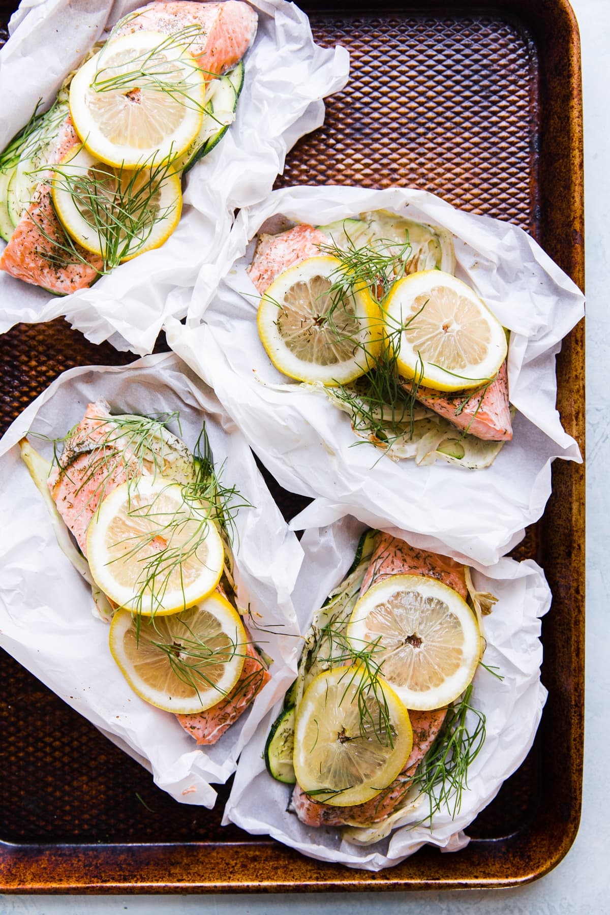 salmon in parchment paper pouches opened and topped with lemon and fennel and dill