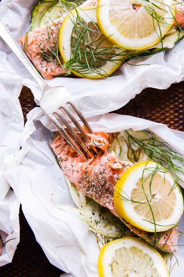 salmon in parchment paper pouches opened and topped with lemon and fennel and dill with a fork