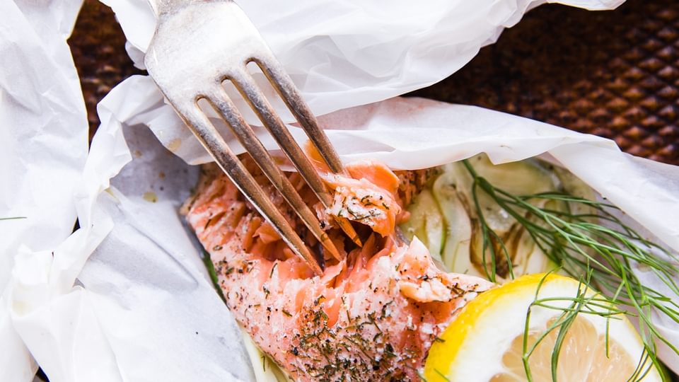 salmon in parchment paper pouches opened and topped with lemon and fennel and dill with a fork
