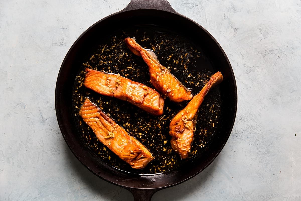 4 four ounce salmon fillets cooking in teriyaki sauce in cast iron pan