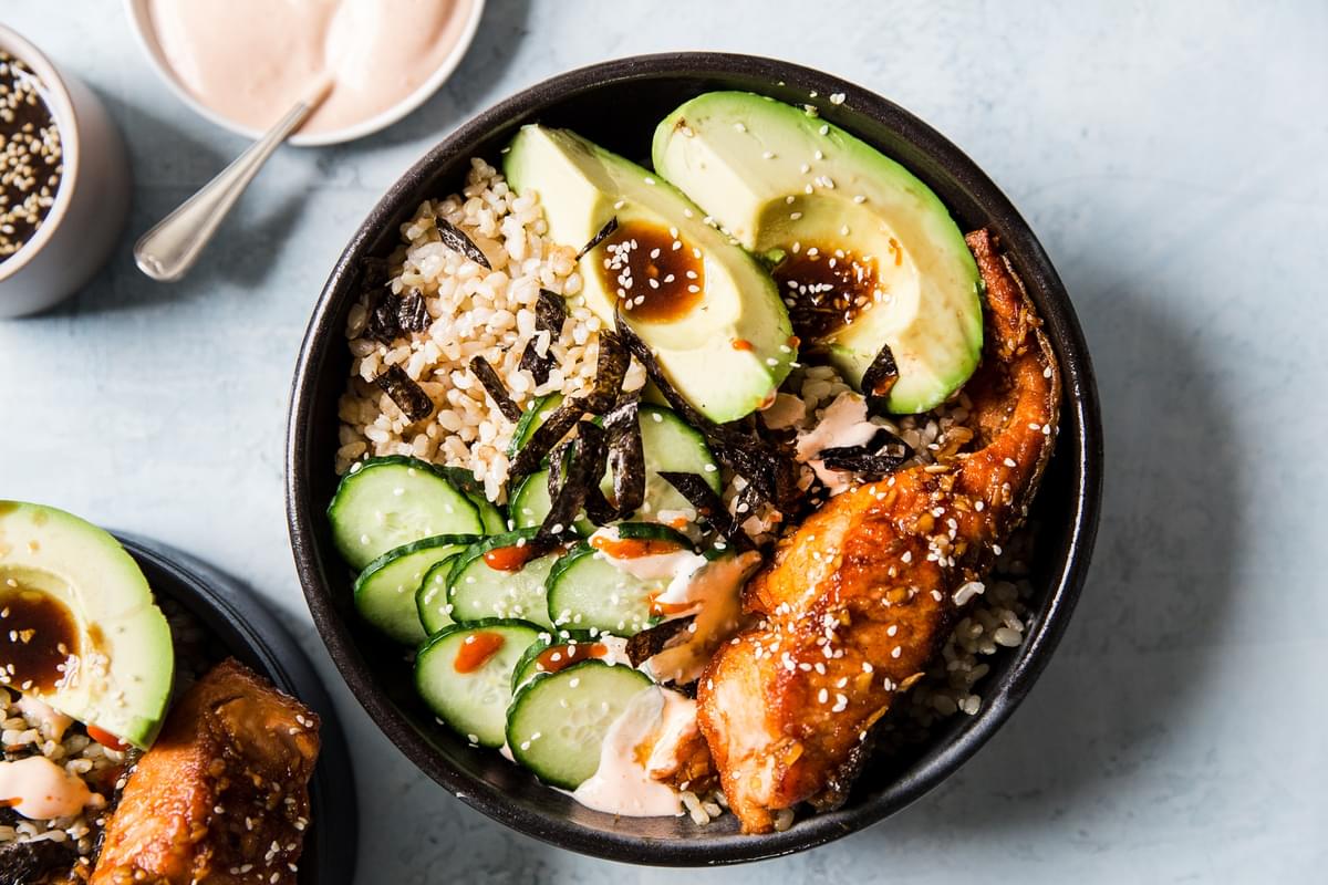 Salmon Sushi Bowl with brown rice, avocado, cucumber and nori topped with sriracha mayonnaise and sesame seeds