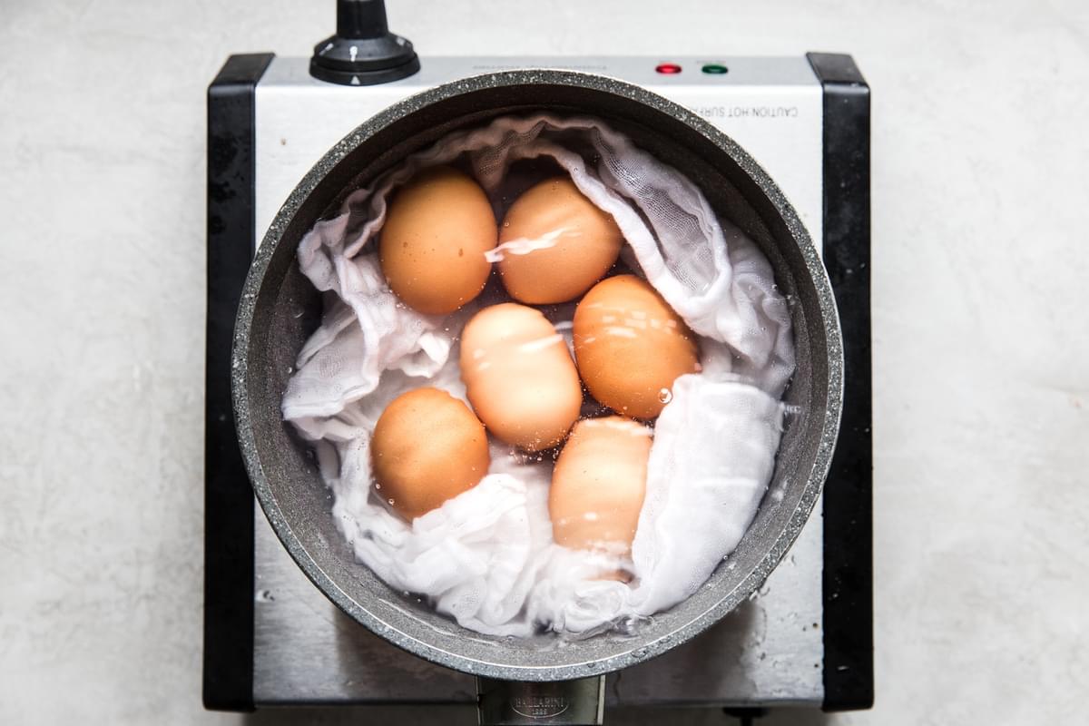 sauce pan of boil water lined with a tea towel holding six brown eggs