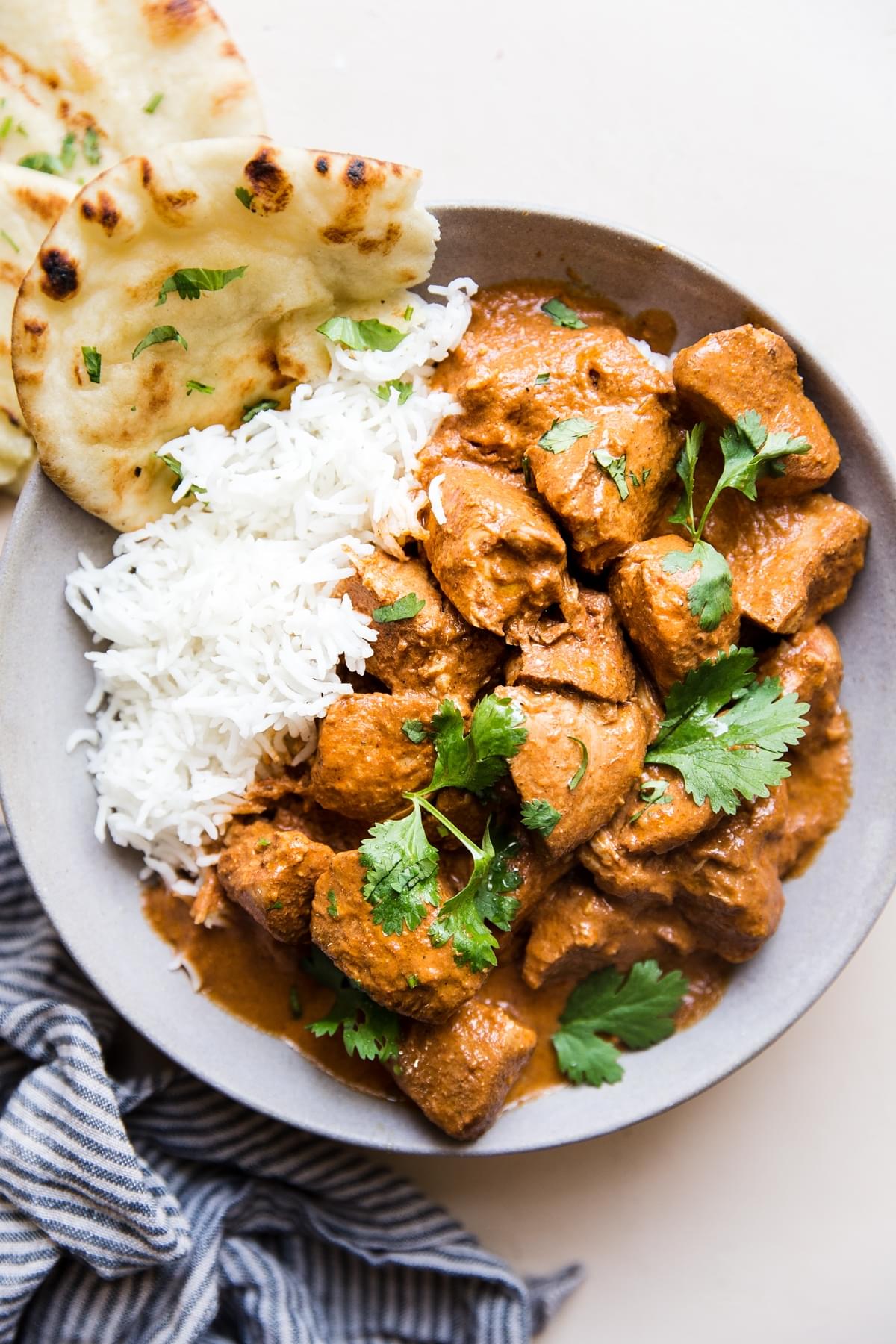 slow cooker butter chicken over white rice in a ceramic bowl served with naan and fresh cilantro