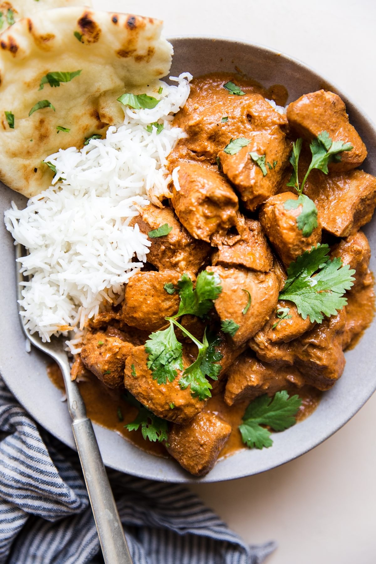 slow cooker butter chicken in a bowl over white rice with naan and fresh cilantro