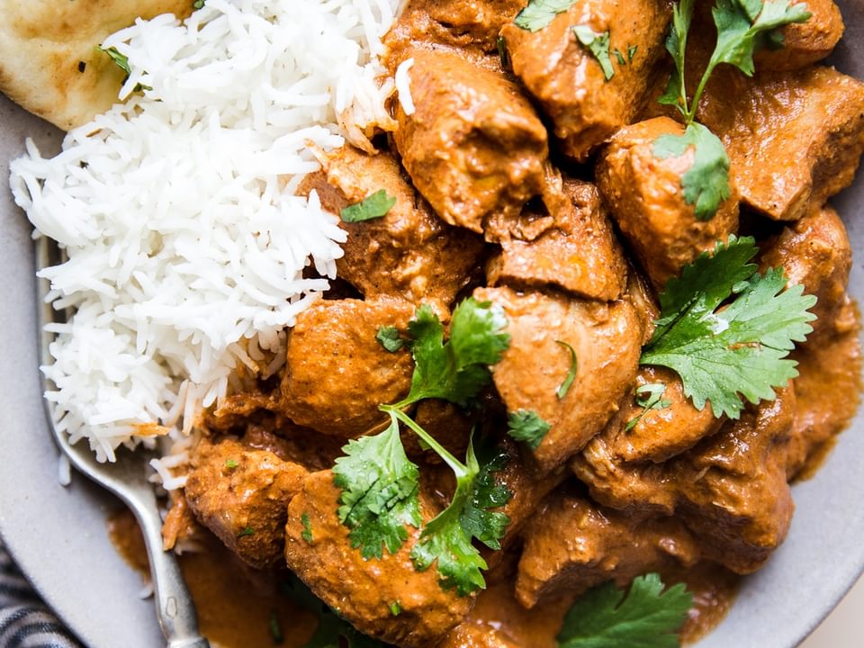 slow cooker butter chicken in a bowl over white rice with naan and fresh cilantro