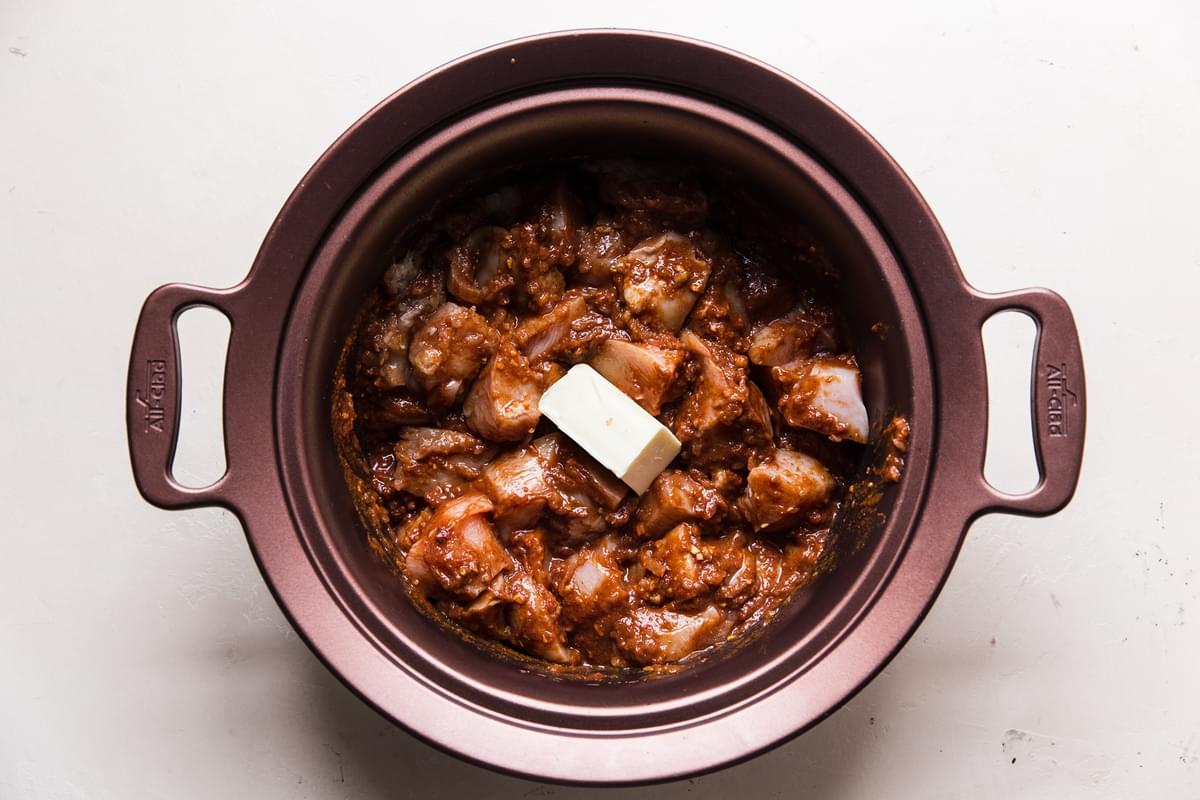raw chicken mixed together with tomato paste and spices topped with butter in a slow cooker