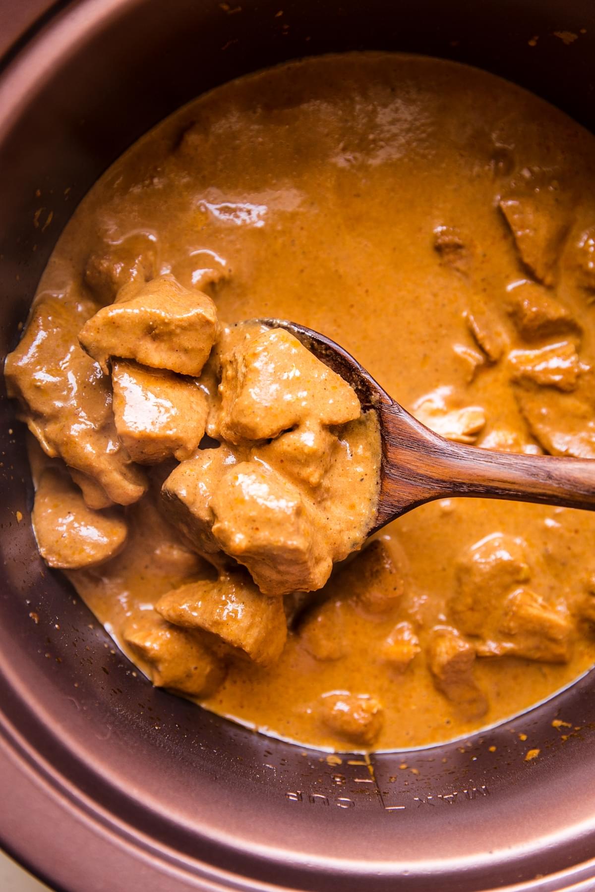 slow cooker butter chicken being scooped out of a crock pot with a wooden spoon