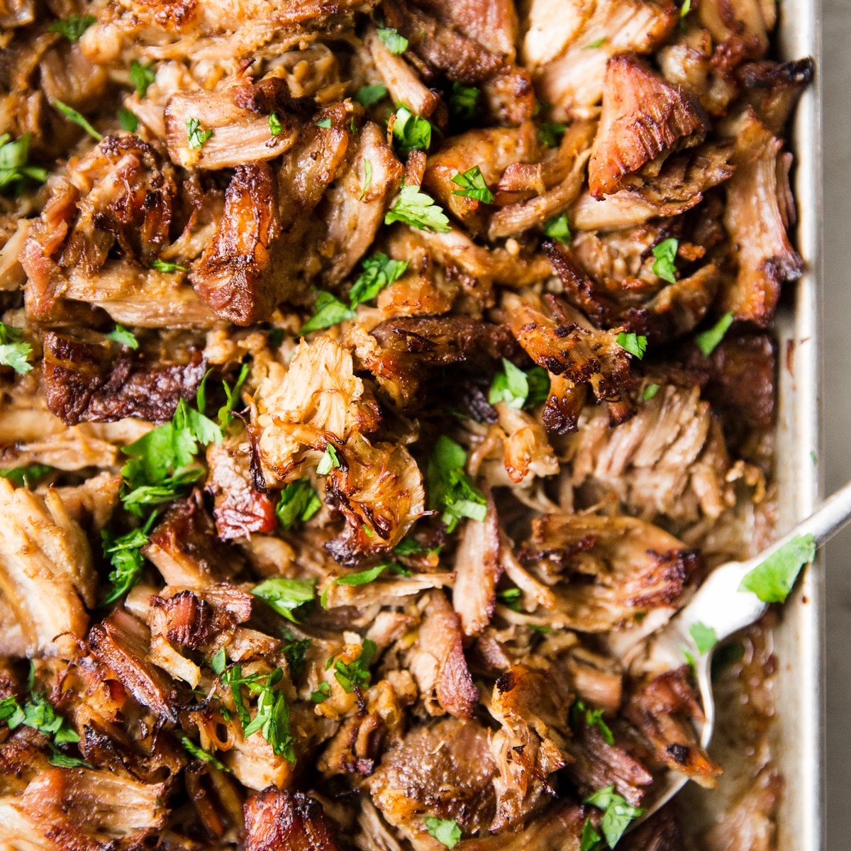 Slow Cooker Crispy Carnitas on a pan with a serving spoon