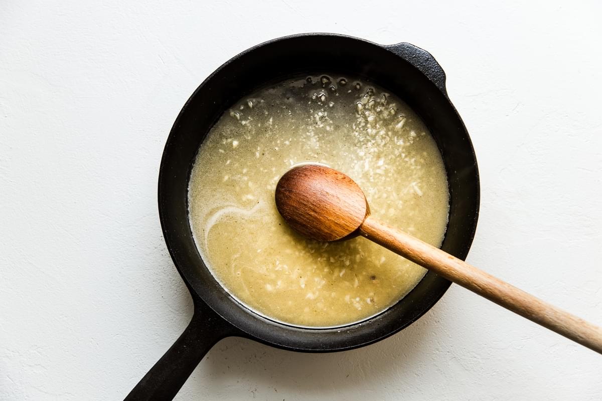 Chicken stock, butter and garlic in a pan with a wooden spoon.