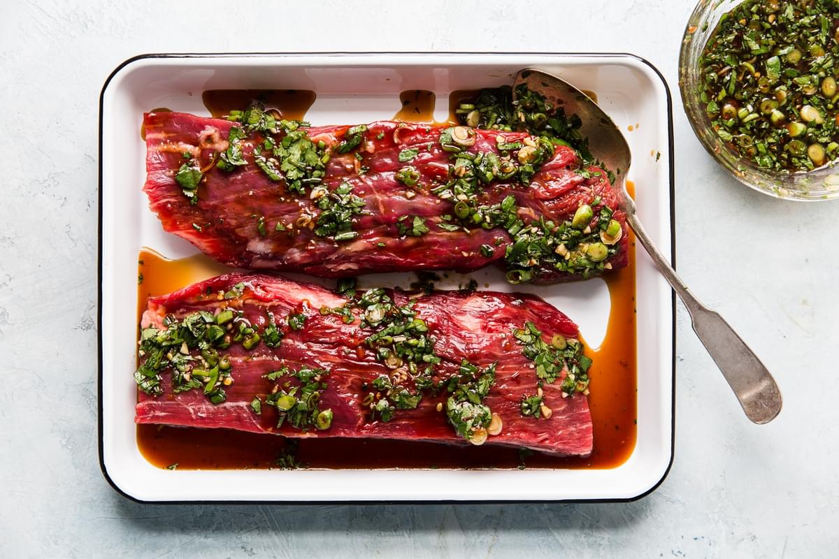 raw flank steak marinating in a pan with soy sauce and fresh scallions