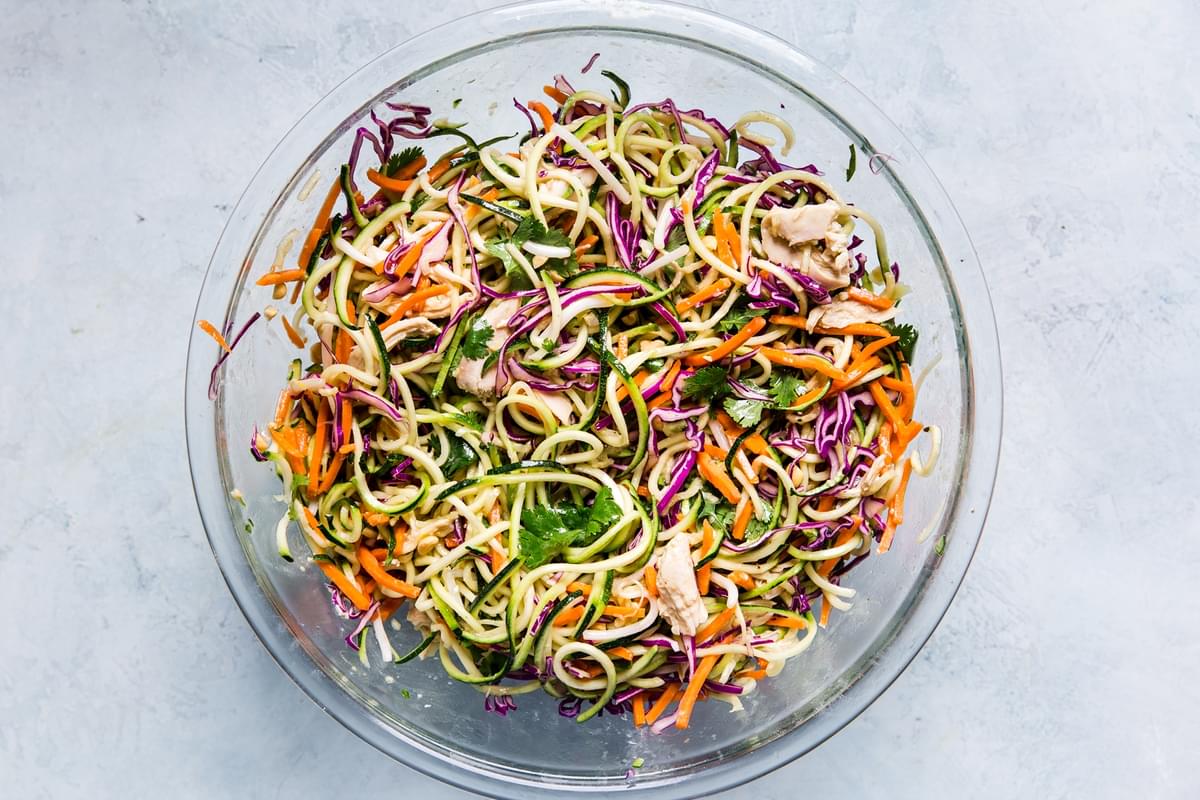 Ingredients for Thai zoodle salad tossed together in a large glass bowl