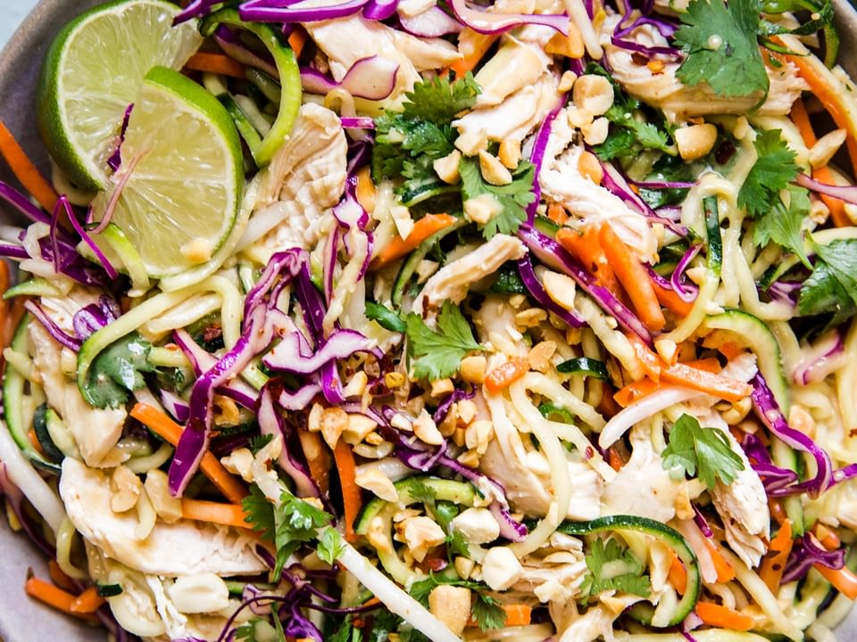 Thai Zoodle salad with chicken, peanuts, and fresh limes in a grey ceramic bowl