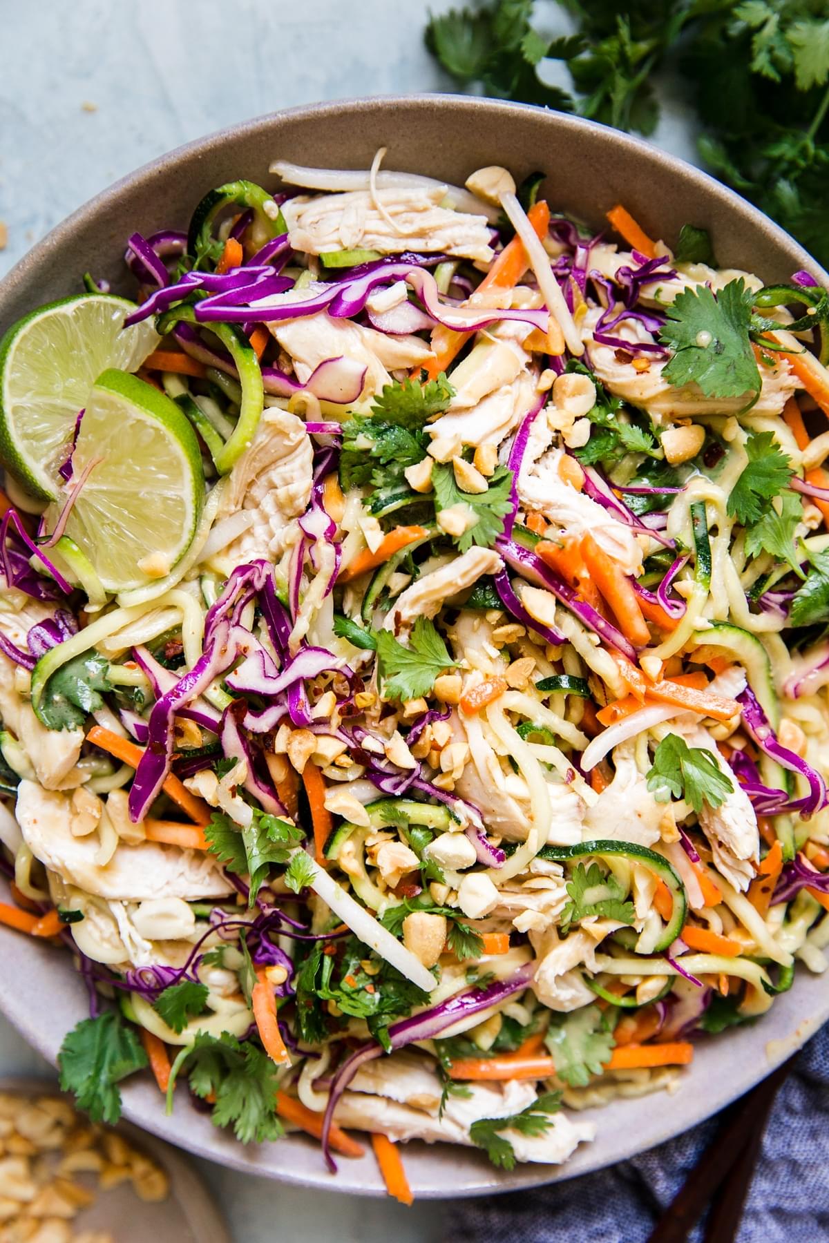 Thai Zucchini noodle salad with chicken, peanuts, and fresh limes in a bowl