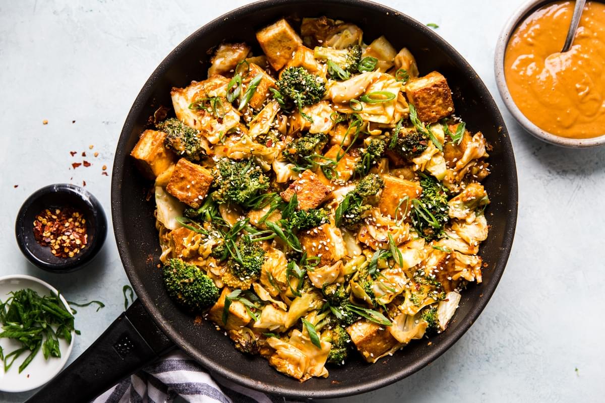 Tofu Stir-Fry with Peanut Sauce and broccoli in a pan with extra sauce in a bowl with a spoon