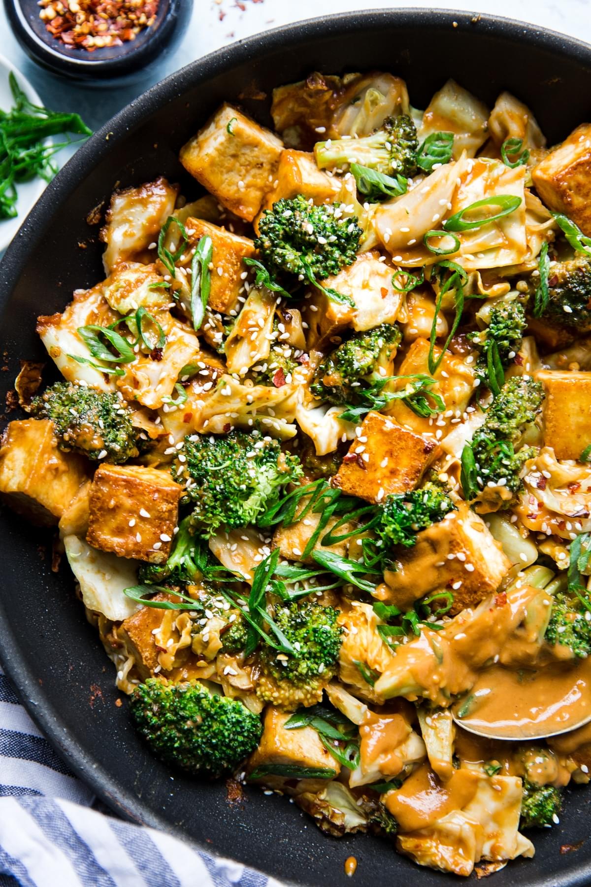 Tofu Stir Fry With Broccoli, Cabbage and peanut sauce in a pan with serving spoon.